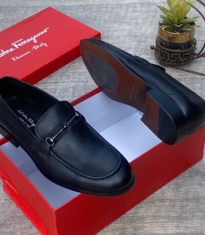 A pair of luxurious black Salvatore Ferragamo loafers, one placed inside a red shoe box and the other beside it, showcasing the high-quality leather and sleek design.