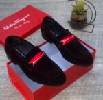 A pair of luxurious black Salvatore Ferragamo loafers with a distinctive red strap and gold buckle, presented in an open red shoe box.