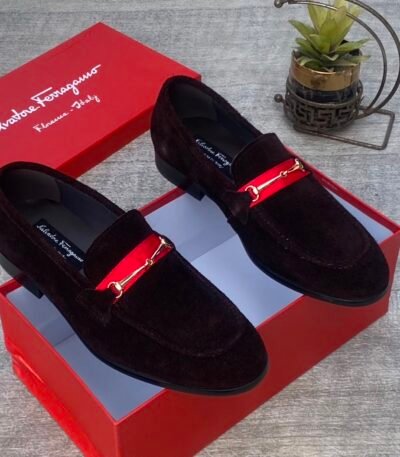 A pair of luxurious black Salvatore Ferragamo loafers with a distinctive red strap and gold buckle, presented in an open red shoe box.