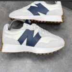 A pair of pristine white New Balance sneakers with navy blue 'N' logo and gum soles, exuding luxury and sophistication.