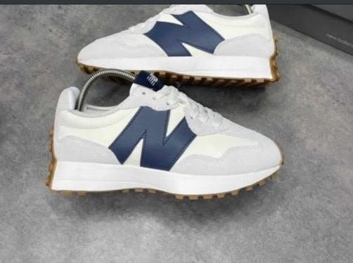A pair of pristine white New Balance sneakers with navy blue 'N' logo and gum soles, exuding luxury and sophistication.