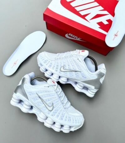 A pair of pristine white Nike sneakers with silver accents, accompanied by a red and white Nike shoe box and an extra pair of insoles, exuding luxury and style.