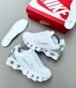 A pair of pristine white Nike sneakers with silver accents, accompanied by a red and white Nike shoe box and an extra pair of insoles, exuding luxury and style.