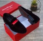 A pair of luxurious black Salvatore Ferragamo loafers with a distinctive red strap and gold buckle, presented in an open red shoe box.
