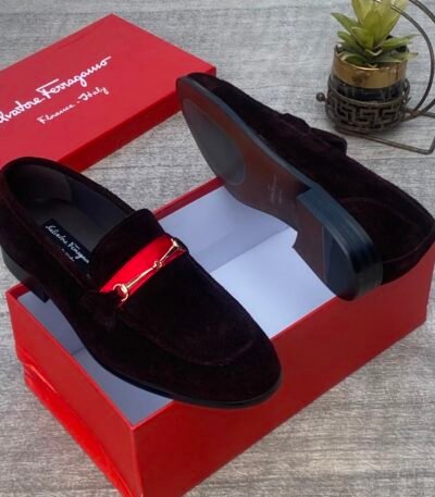 A pair of luxurious black Salvatore Ferragamo loafers with a distinctive red strap and gold buckle, presented in an open red shoe box.