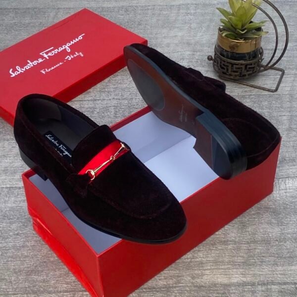 A pair of luxurious black Salvatore Ferragamo loafers with a distinctive red strap and gold buckle, presented in an open red shoe box.
