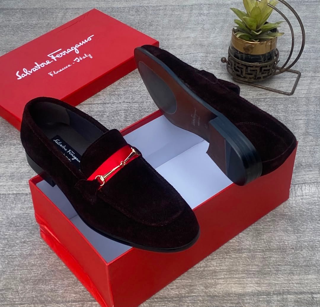 root A pair of luxurious black Salvatore Ferragamo loafers with a distinctive red strap and gold buckle, presented in an open red shoe box.