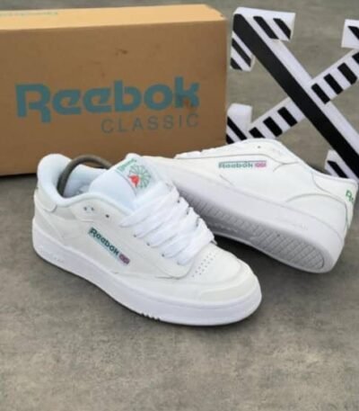 A pair of pristine white Reebok Classic sneakers with colorful accents, displayed with their box on a sleek grey surface.