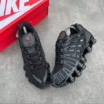 A pair of sleek black Nike sneakers with red accents, positioned next to a red Nike shoe box on a grey surface.