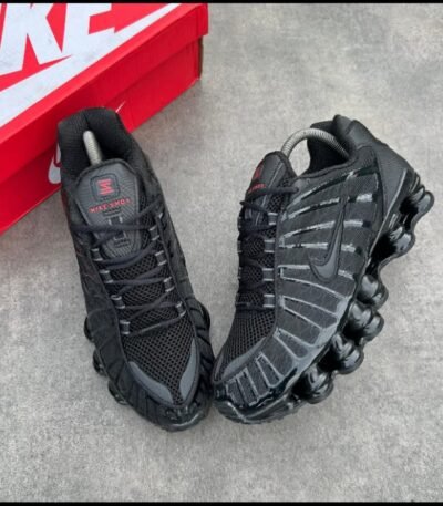 A pair of sleek black Nike sneakers with red accents, positioned next to a red Nike shoe box on a grey surface.