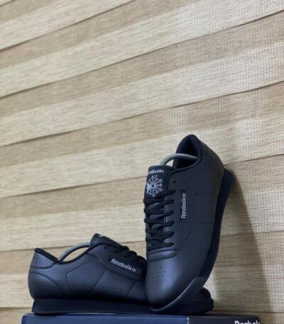 A pair of sleek black Reebok shoes with white logo on a navy box