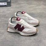 A pair of luxurious white and maroon New Balance sneakers with gum soles, displayed on a grey surface with a shoe box in the background.