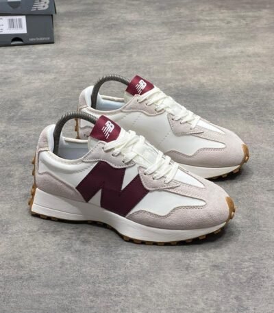 A pair of luxurious white and maroon New Balance sneakers with gum soles, displayed on a grey surface with a shoe box in the background.