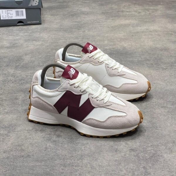 A pair of luxurious white and maroon New Balance sneakers with gum soles, displayed on a grey surface with a shoe box in the background.