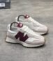A pair of luxurious white and maroon New Balance sneakers with gum soles, displayed on a grey surface with a shoe box in the background.