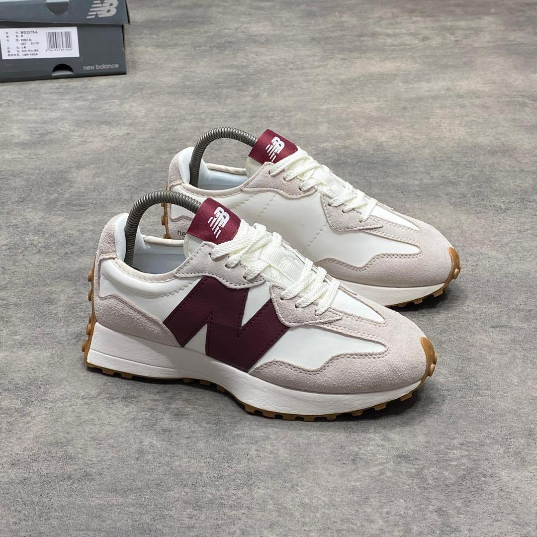 root A pair of luxurious white and maroon New Balance sneakers with gum soles, displayed on a grey surface with a shoe box in the background.