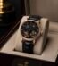 A luxurious Patek Philippe watch with a black face and rose gold casing, displayed on a beige cushion within an open watch box.