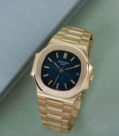 A luxurious gold Patek Philippe watch with a blue face, displayed on a green surface.