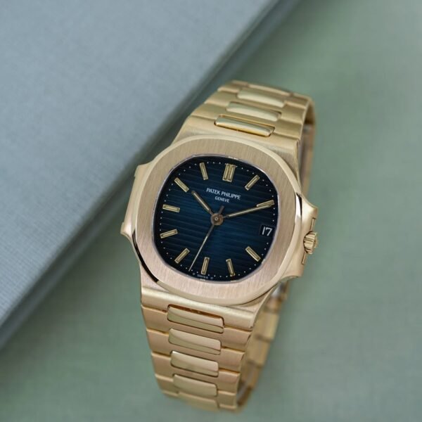 A luxurious gold Patek Philippe watch with a blue face, displayed on a green surface.