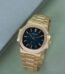 A luxurious gold Patek Philippe watch with a blue face, displayed on a green surface.