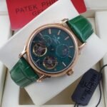 A luxurious Patek Philippe watch with a green face and leather strap, presented in a white box with a red card.