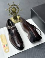 A pair of black leather monk strap shoes on a white cloth, accompanied by a shoe tree and a decorative ship's wheel, exuding luxury and refinement.