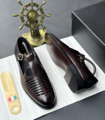 A pair of black leather monk strap shoes on a white cloth, accompanied by a shoe tree and a decorative ship's wheel, exuding luxury and refinement.