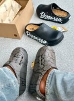 A pair of stylish clogs in black and grey marble finish, showcasing the brand name and logo.