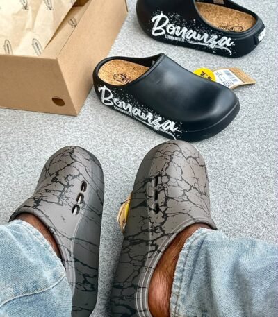 A pair of stylish clogs in black and grey marble finish, showcasing the brand name and logo.