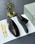 A pair of luxurious black leather half shoes displayed on a white surface, and a decorative gold ship's wheel, exuding elegance and refinement.