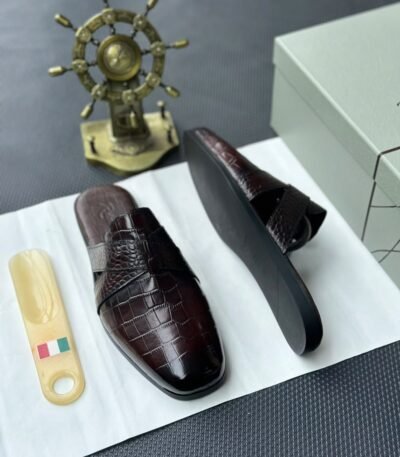 A pair of luxurious black leather half shoes displayed on a white surface, and a decorative gold ship's wheel, exuding elegance and refinement.