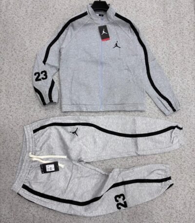 A luxurious black Nike tracksuit with grey stripes, laid out on a grey surface, showcasing its sleek design and iconic logo.