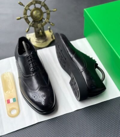 A pair of luxurious black leather oxford shoes with brogue detailing, presented on a crisp white background with a green box and golden accents, evoking a sense of high-end style and sophistication.