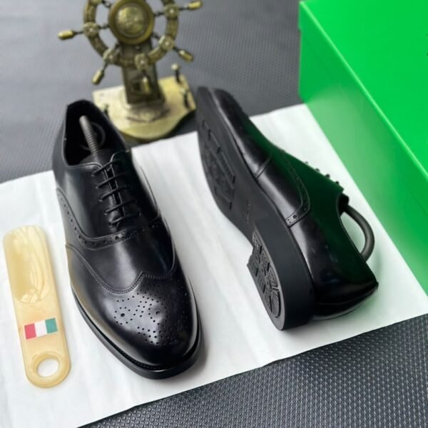 A pair of luxurious black leather oxford shoes with brogue detailing, presented on a crisp white background with a green box and golden accents, evoking a sense of high-end style and sophistication.