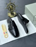 A pair of luxurious black leather half shoes displayed on a white surface, and a decorative gold ship's wheel, exuding elegance and refinement.