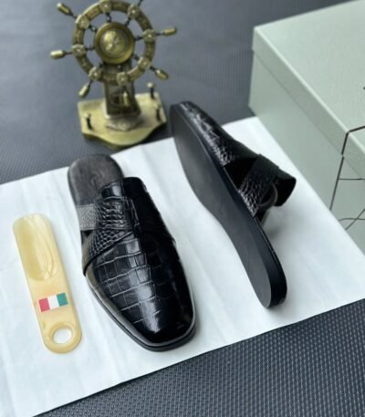 A pair of luxurious black leather half shoes displayed on a white surface, and a decorative gold ship's wheel, exuding elegance and refinement.