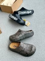 A pair of stylish clogs in black and grey marble finish, showcasing the brand name and logo.