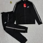 A luxurious black Nike tracksuit with grey stripes, laid out on a grey surface, showcasing its sleek design and iconic logo.