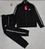 A luxurious black Nike tracksuit with grey stripes, laid out on a grey surface, showcasing its sleek design and iconic logo.