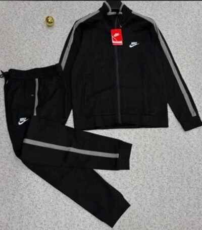 A luxurious black Nike tracksuit with grey stripes, laid out on a grey surface, showcasing its sleek design and iconic logo.