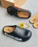 A pair of stylish clogs in black and grey marble finish, showcasing the brand name and logo.