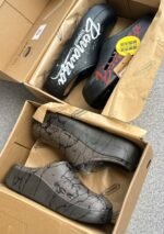 A pair of stylish clogs in black and grey marble finish, showcasing the brand name and logo.