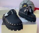 A pair of luxurious green half shoes with metallic studs and a silver buckle, showcased on a cream-colored shoe box.