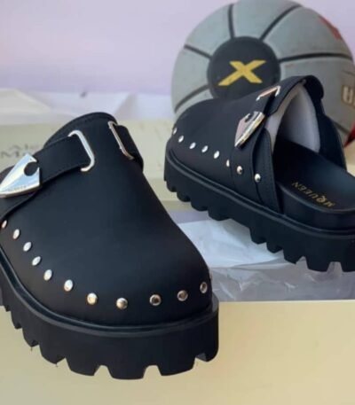 A pair of luxurious green half shoes with metallic studs and a silver buckle, showcased on a cream-colored shoe box.