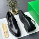 A pair of luxurious black leather loafers showcased on a pristine white surface, accompanied by a sleek shoe tree and a vibrant green box, evoking a sense of high-end sophistication.