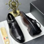 A pair of black leather monk strap shoes on a white cloth, accompanied by a shoe tree and a decorative ship's wheel, exuding luxury and refinement.