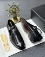 A pair of black leather monk strap shoes on a white cloth, accompanied by a shoe tree and a decorative ship's wheel, exuding luxury and refinement.