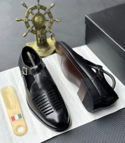 A pair of black leather monk strap shoes on a white cloth, accompanied by a shoe tree and a decorative ship's wheel, exuding luxury and refinement.